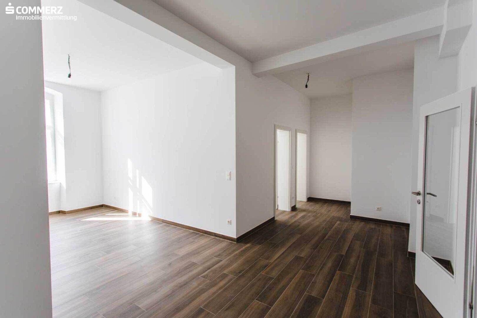 Großer, heller Wohnbereich mit Laminatboden und mehreren Türen, ideal für offenes Wohnen.