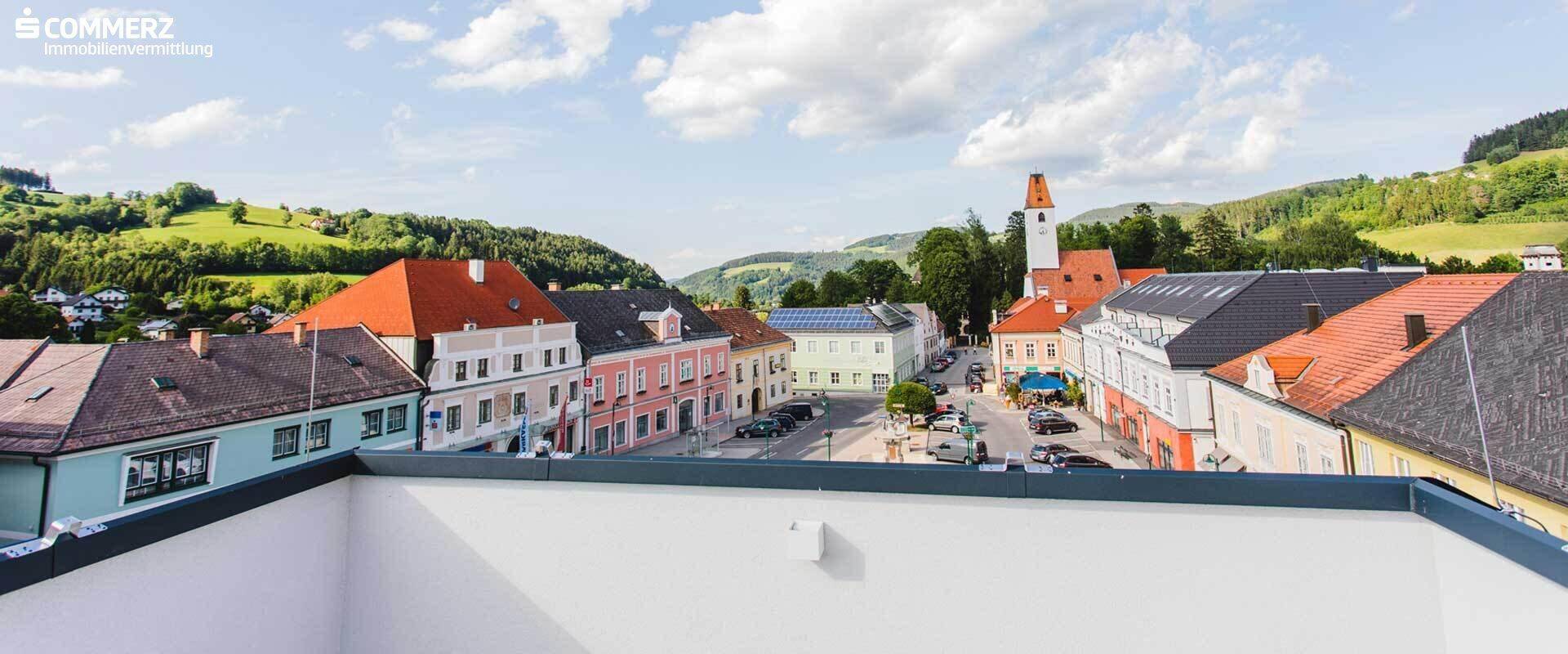 Weitläufiger Blick über die Dächer der Stadt und die umliegende grüne Hügellandschaft.