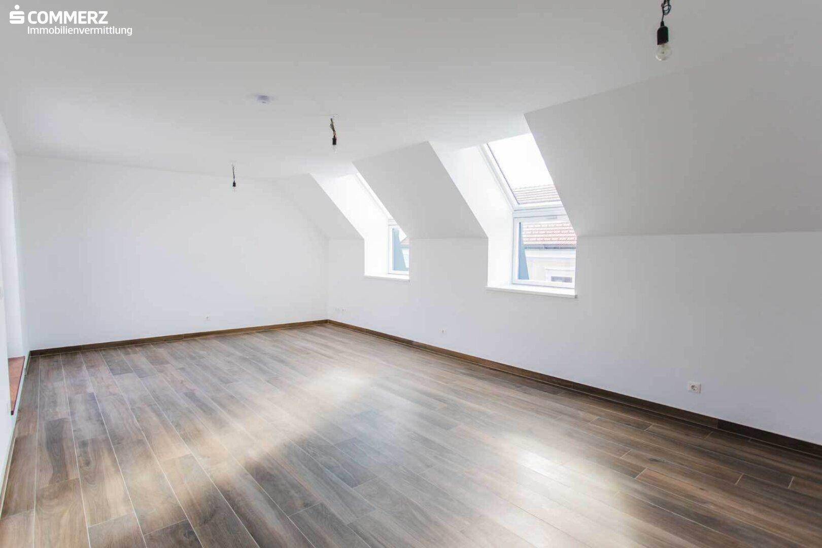Geräumiger Dachbodenraum mit Laminatboden, weißen Wänden und mehreren Dachfenstern.