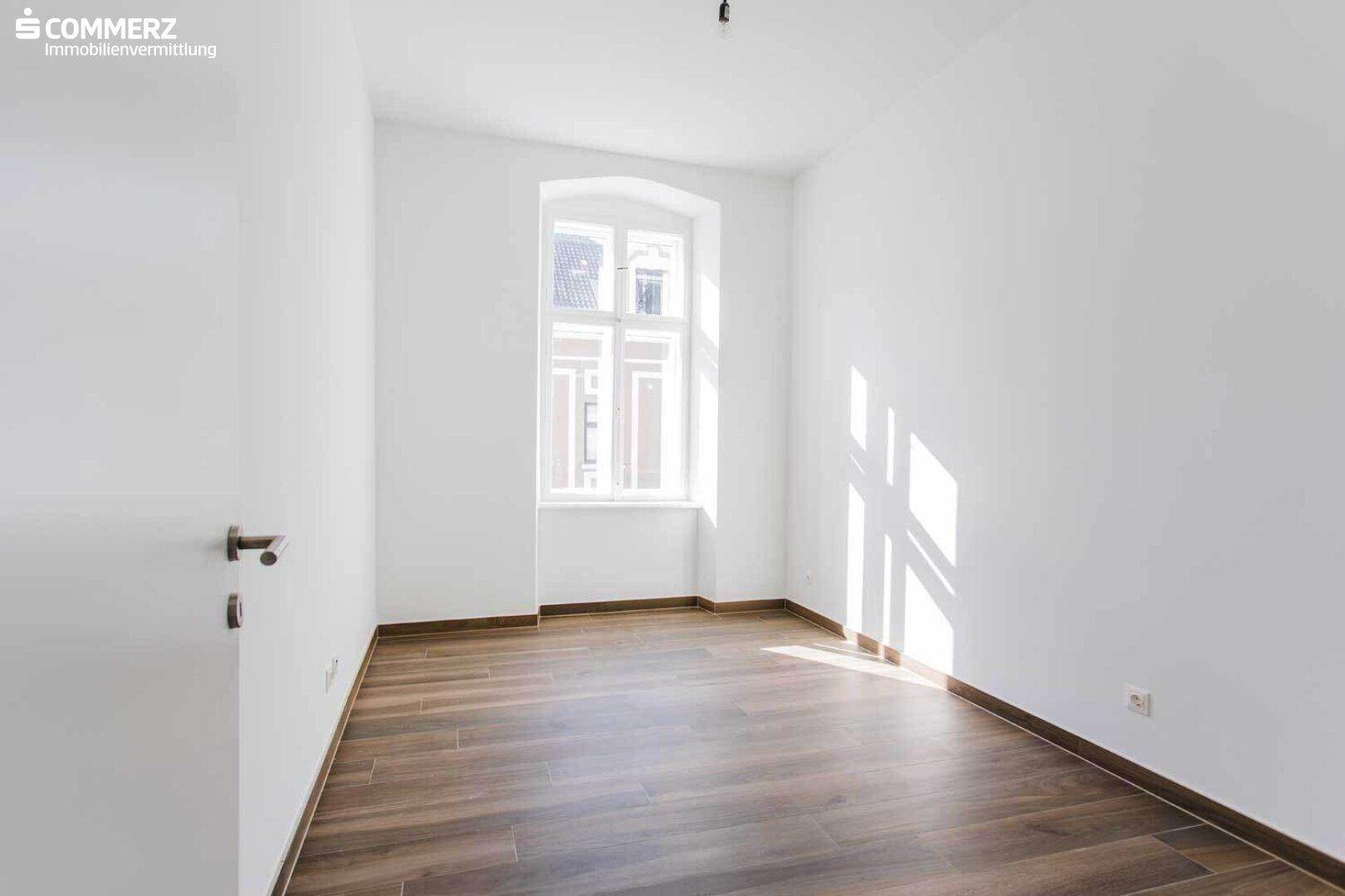 Unmöbliertes Schlafzimmer mit Laminatboden und weiß gestrichenen Wänden, hell und einladend.
