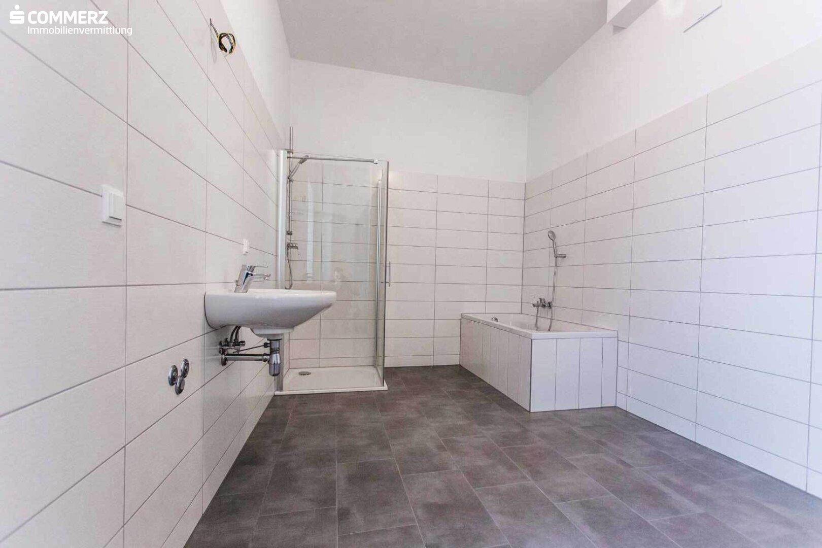 Geräumiges Badezimmer mit weißen Wandfliesen, dunklem Boden, Dusche und Badewanne.