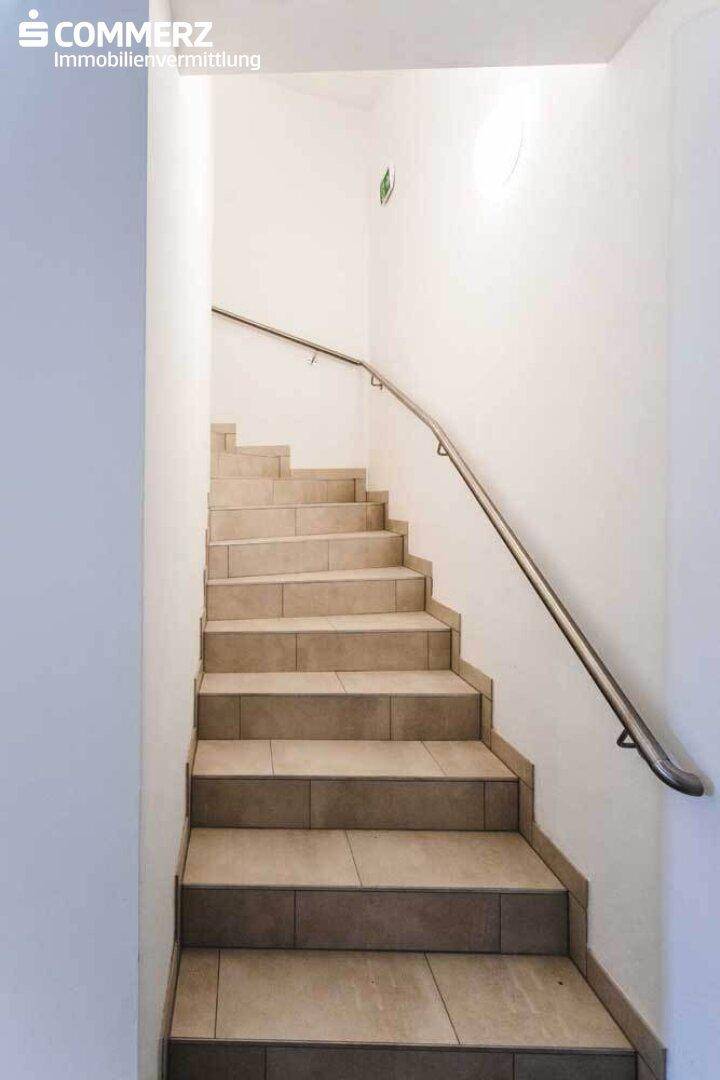 Heller Treppenaufgang mit Fliesenstufen und einem schlichten Metallgeländer in einem modernen Gebäude.