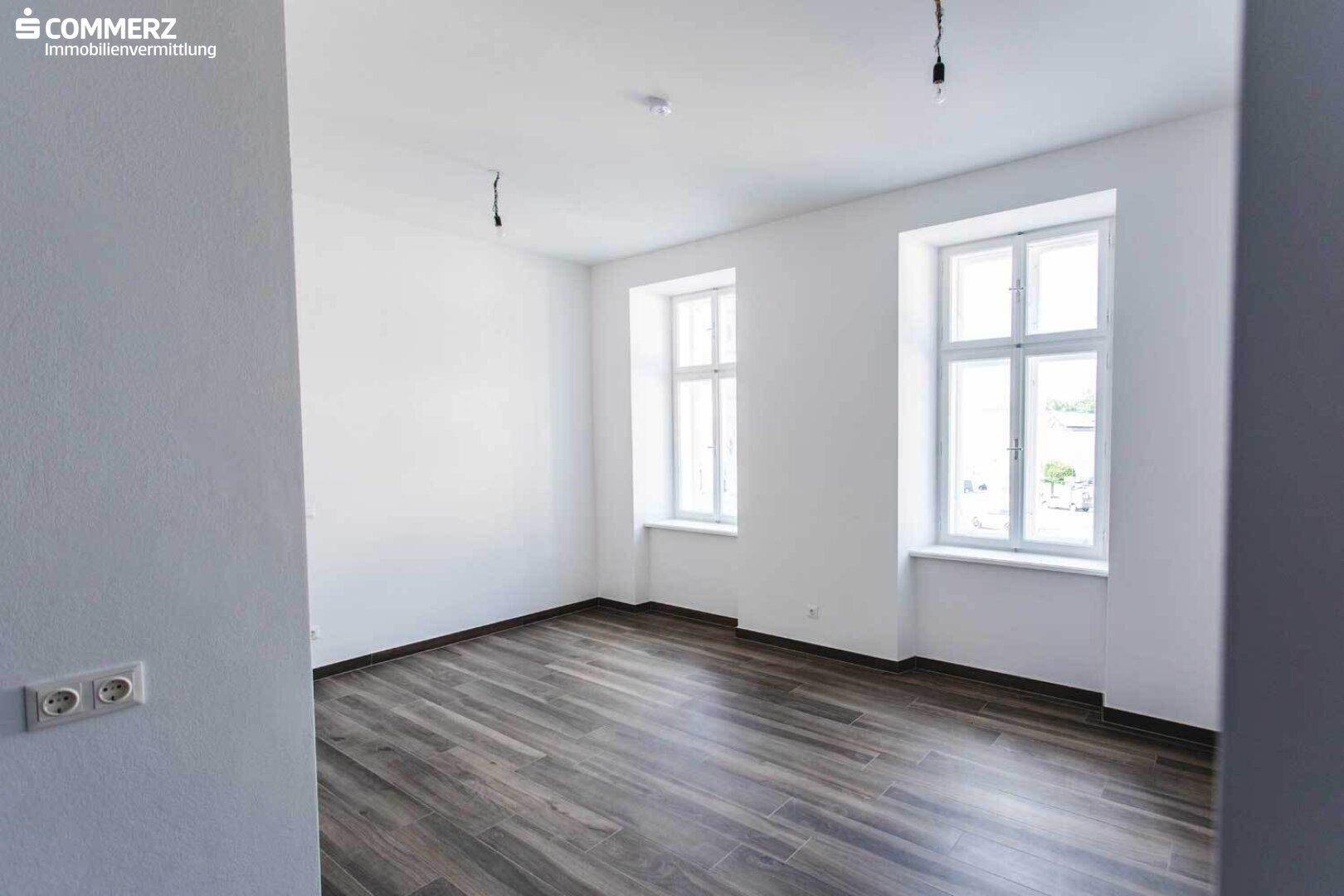 Heller, leerer Raum mit modernem Laminatboden und großen Fenstern, bereit zur individuellen Gestaltung.