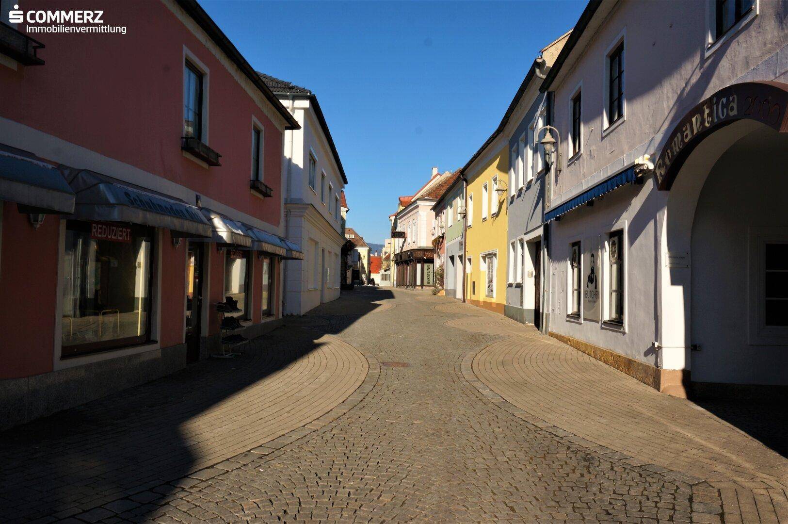 Historische Gasse mit Kopfsteinpflaster, gesäumt von farbenfrohen Gebäuden unter blauem Himmel.