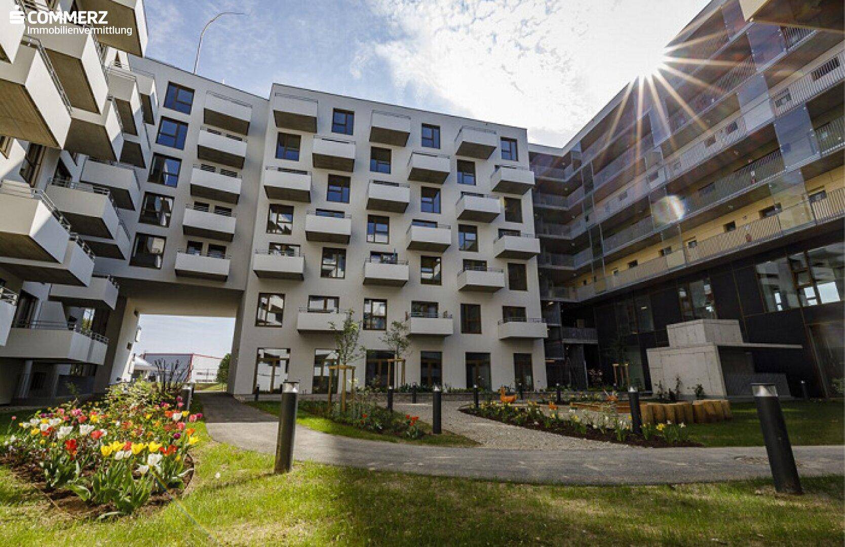 Moderne Wohnanlage mit mehreren Gebäuden, Balkonen und einem begrünten Innenhof mit Blumenbeeten.