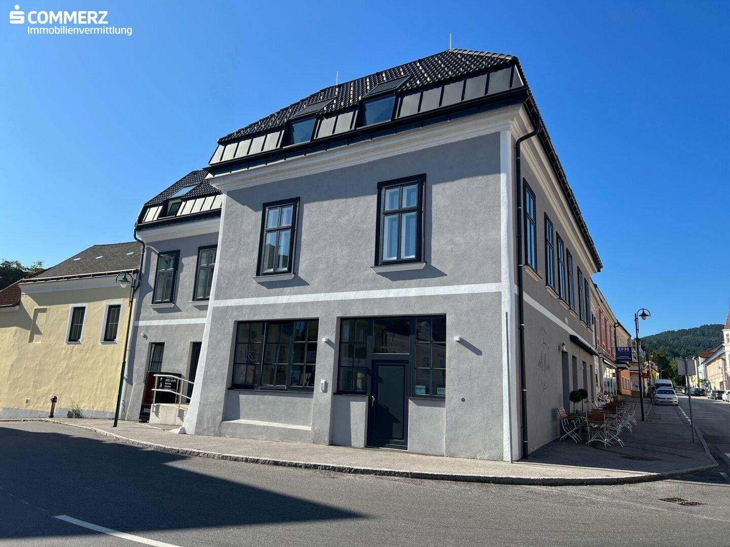 Ansicht des modernen Gebäudes mit grauer Fassade und dunklen Fenstern an einer belebten Straße.