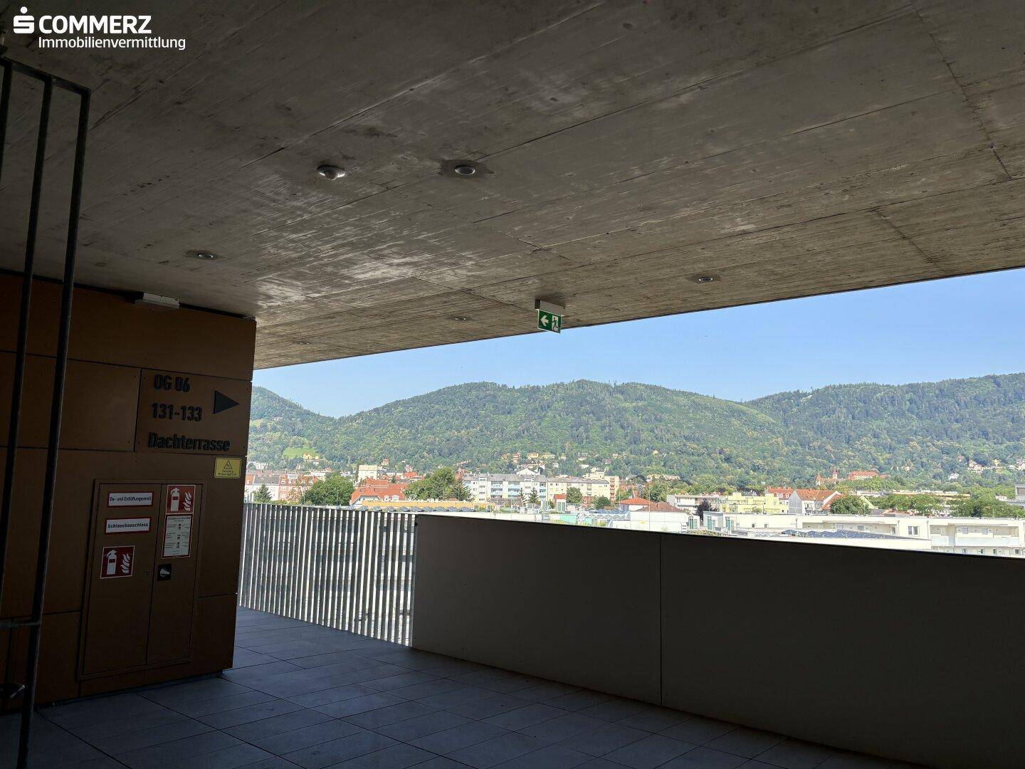 Überdachter Außenbereich mit Blick auf grüne Hügel und die umliegende Stadtlandschaft.