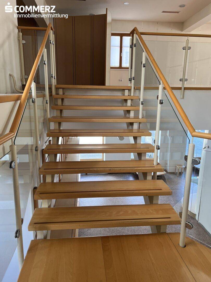 Moderne Holztreppe mit Glasgeländer und Metallpfosten, die verschiedene Ebenen des Gebäudes verbindet.