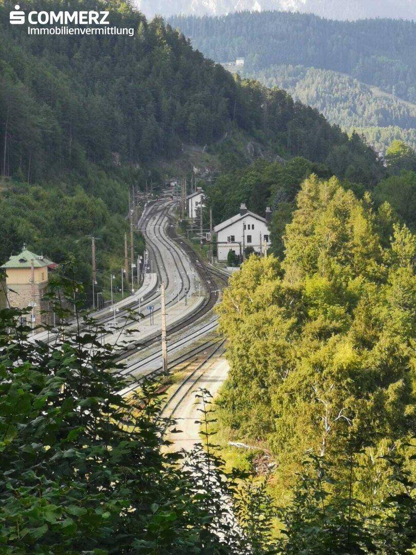 Detailaufnahme einer Eisenbahnstrecke, die sich durch ein bewaldetes Tal mit einem Gebäude schlängelt.