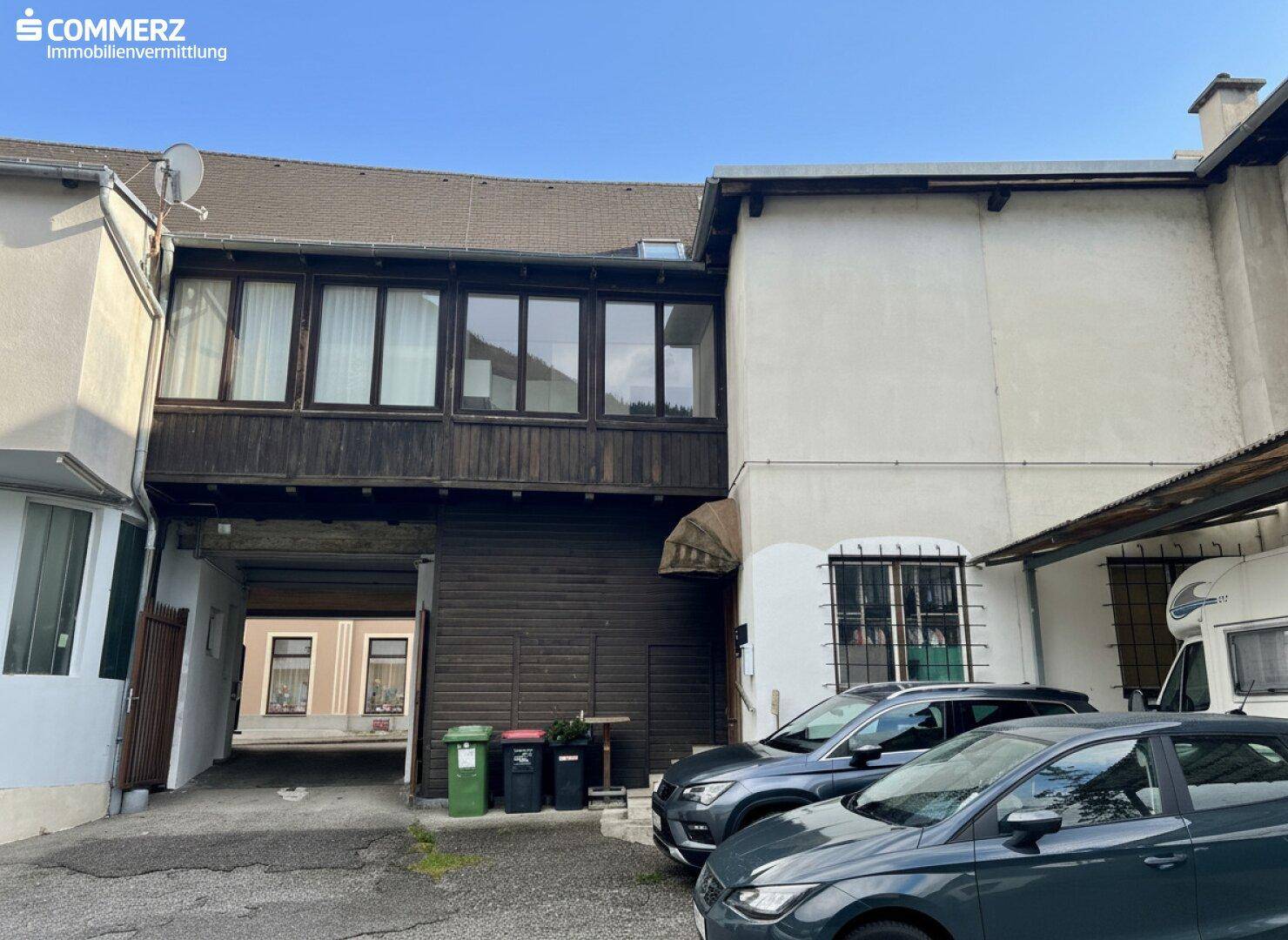 Rückansicht des Gebäudes mit einer überdachten Loggia und geparkten Fahrzeugen im Hof.