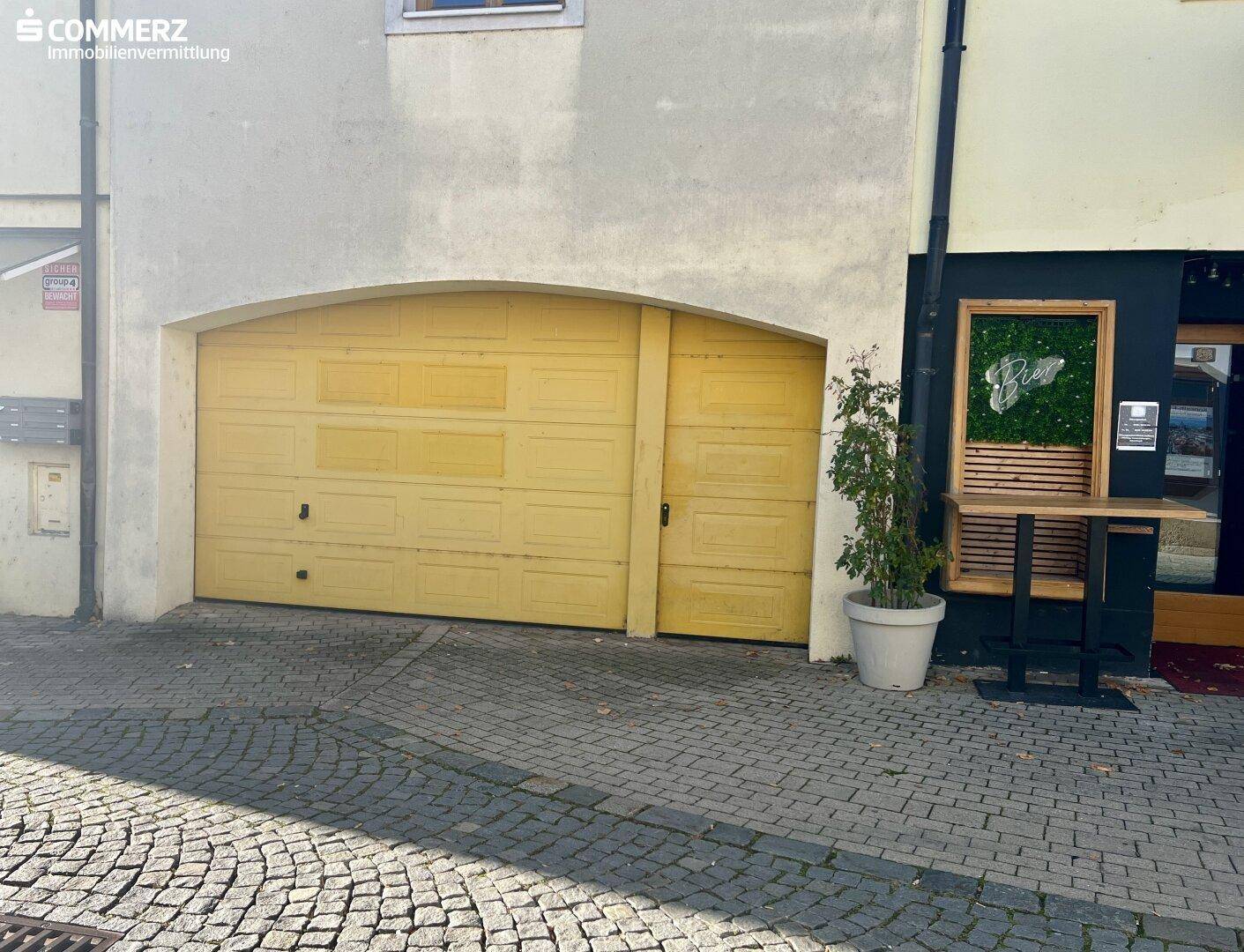 Gelbes Garagentor an einem historischen Gebäude mit Kopfsteinpflaster und angrenzendem Geschäftseingang.