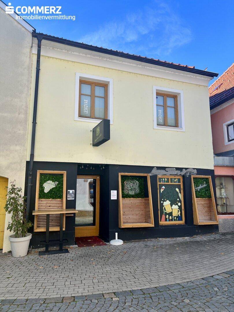 Historisches Gebäude mit dunkler Ladenfront und oberen Fenstern, umgeben von Kopfsteinpflaster.