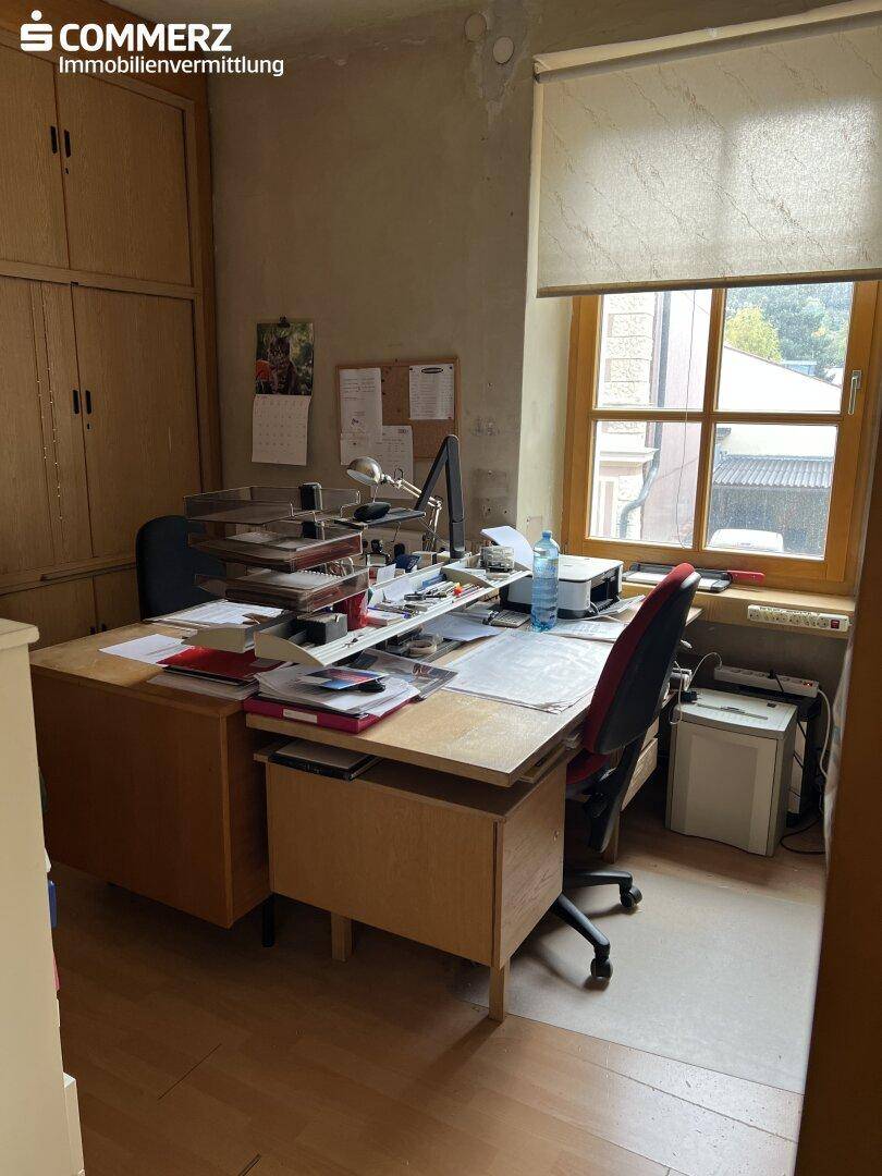 Büro mit Schreibtisch, Bürostuhl, Einbauschränken und einem Fenster mit natürlichem Lichteinfall.