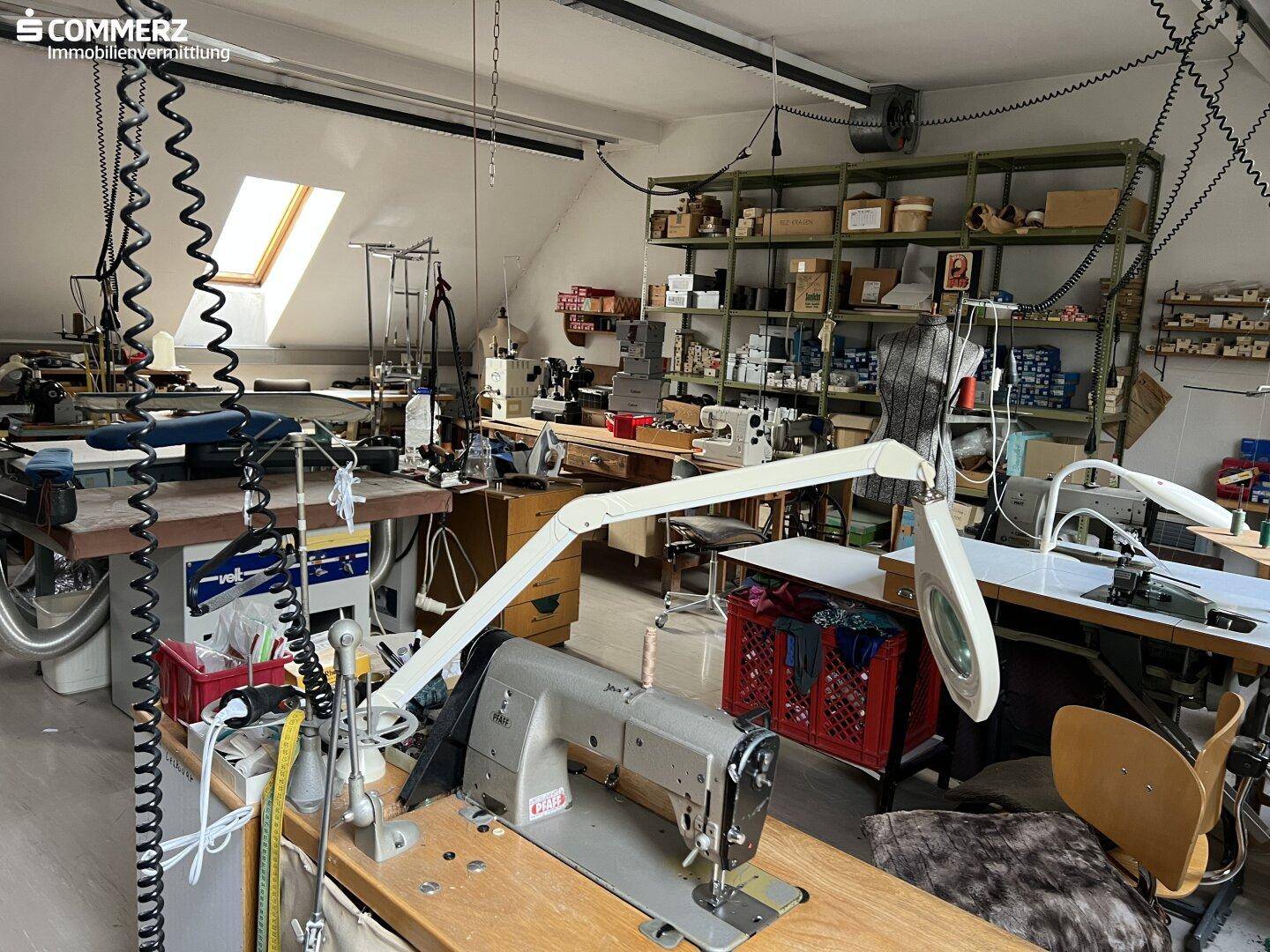 Werkstattraum mit mehreren Nähmaschinen, Regalen und einem Dachfenster für Tageslicht.