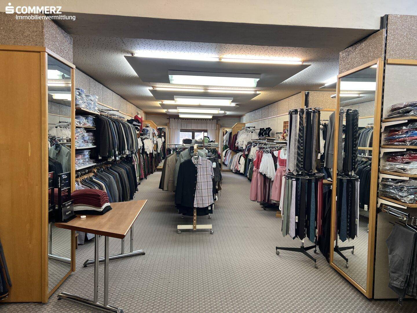 Langer Verkaufsraum mit Kleiderständern, Spiegeln und Teppichboden.