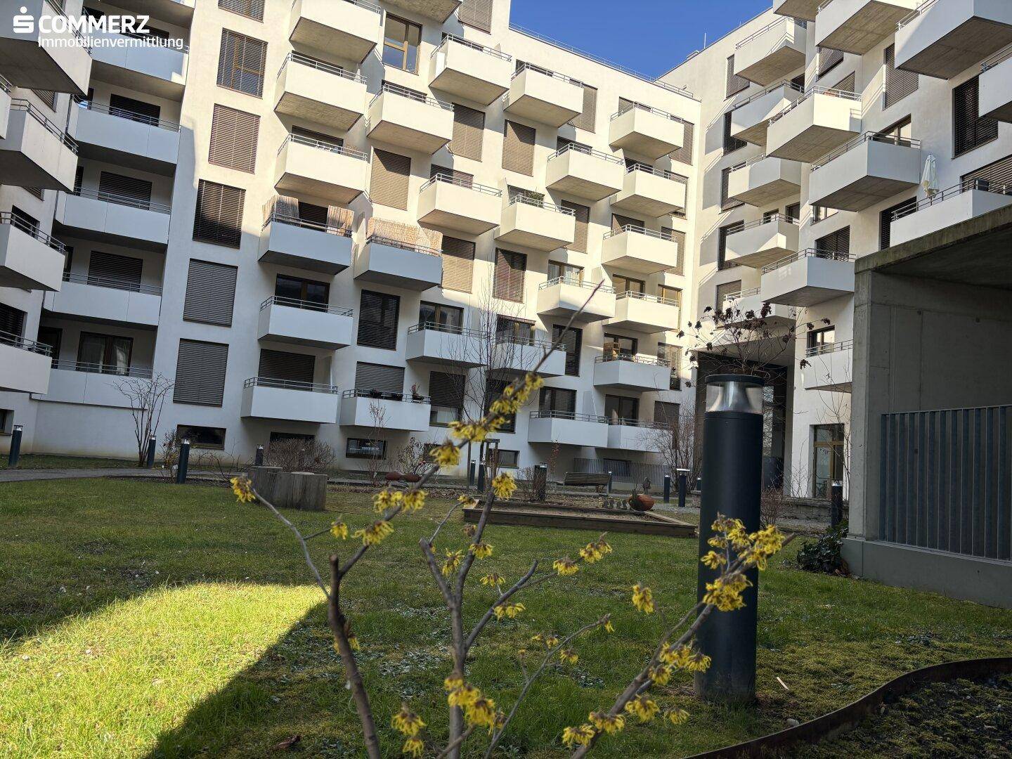 Innenhof eines modernen Wohnkomplexes mit gepflegter Grünfläche und blühenden Sträuchern.