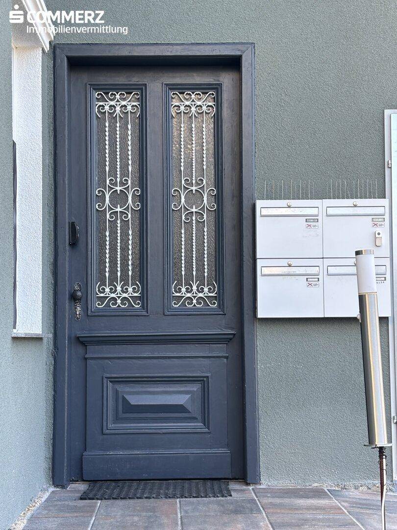 Eingangstür in dunklem Grau mit dekorativen Gittern und Briefkästen an der Hauswand.