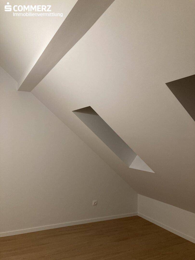 Heller Raum im Dachgeschoss mit schrägen Wänden und sichtbaren Holzbalken an der Decke.