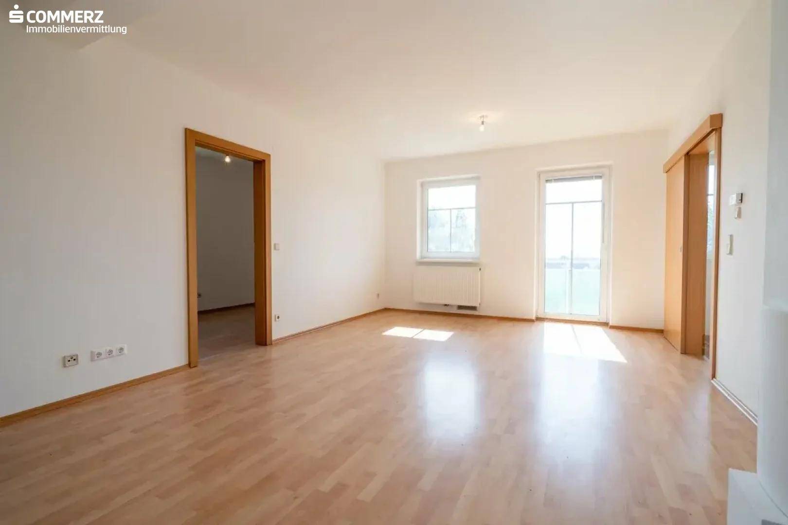 Geräumiges Wohnzimmer mit hellem Laminatboden und viel Tageslicht, bereit zur individuellen Gestaltung.