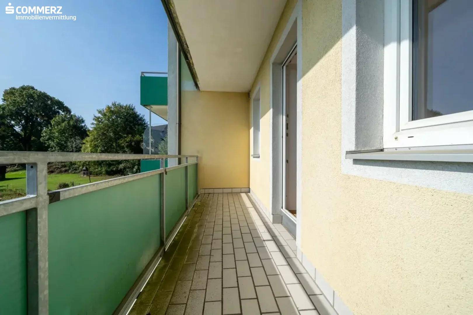 Langer Balkon mit Fliesen und grüner Verkleidung, zugänglich von den Innenräumen.