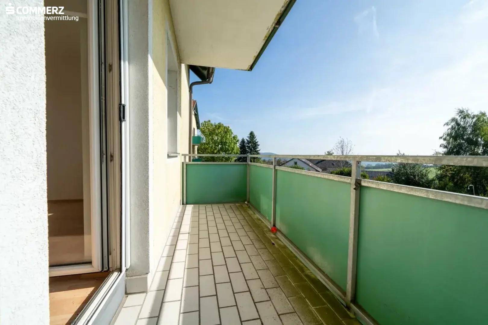 Schmaler Balkon mit Fliesenboden und grüner Brüstung, bietet einen Blick ins Grüne.