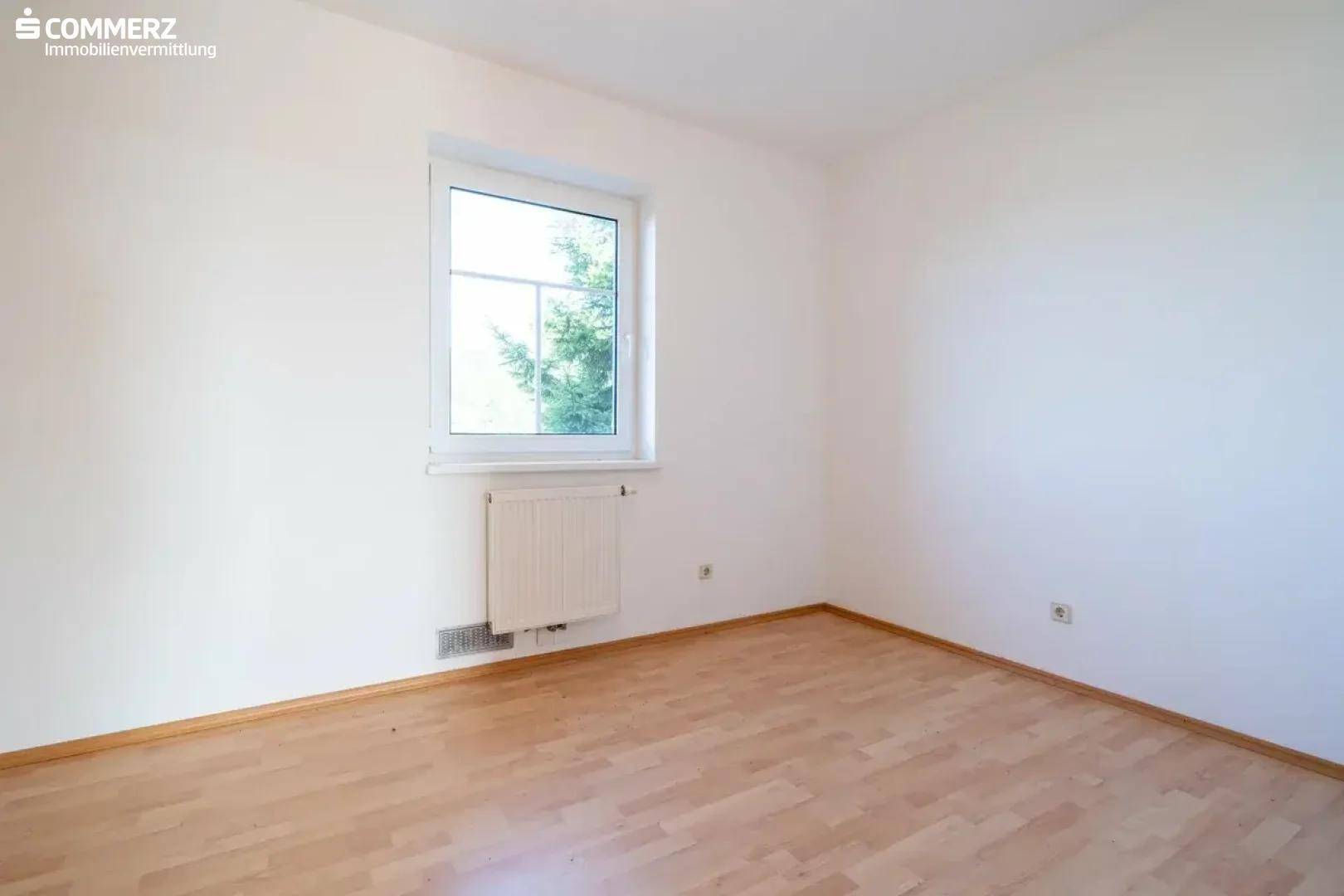 Helles Schlafzimmer mit Laminatboden und großem Fenster, bietet viel Tageslicht.
