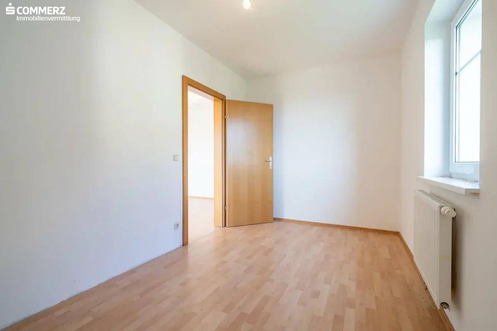 Geräumiges Schlafzimmer mit hellem Laminatboden und Zugang zu weiteren Räumen.
