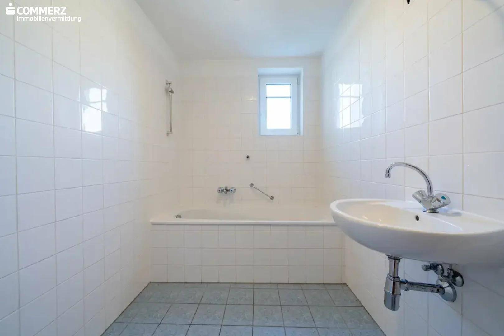 Gefliestes Badezimmer mit Badewanne, Waschbecken und Fenster, in gutem Zustand.