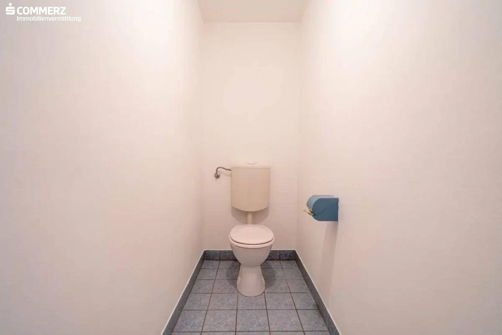 Separates WC mit Toilette und Fliesenboden, in schlichtem, funktionalem Design.