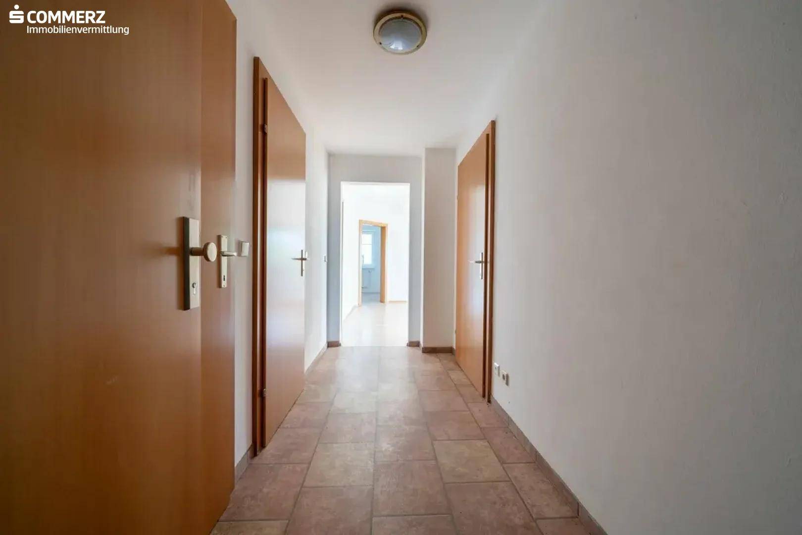 Langer Flur mit Fliesenboden und mehreren Holztüren, verbindet die verschiedenen Räume.
