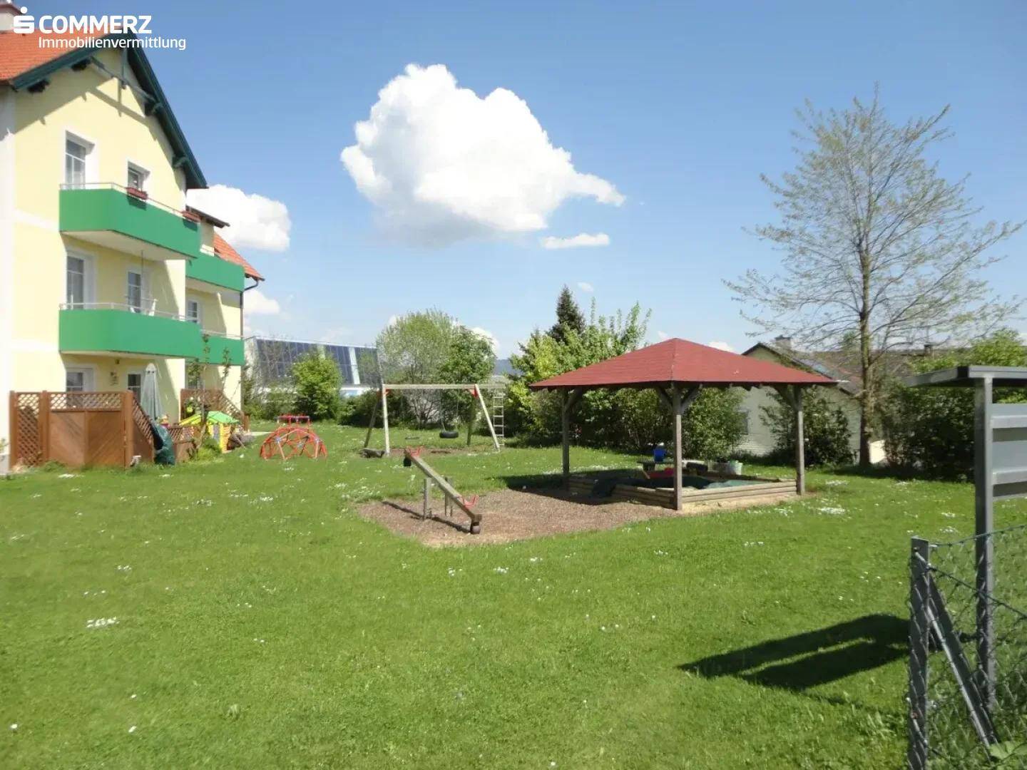 Großer Gemeinschaftsgarten mit Spielplatz, Schaukeln und Sandkasten, ideal für Familien.