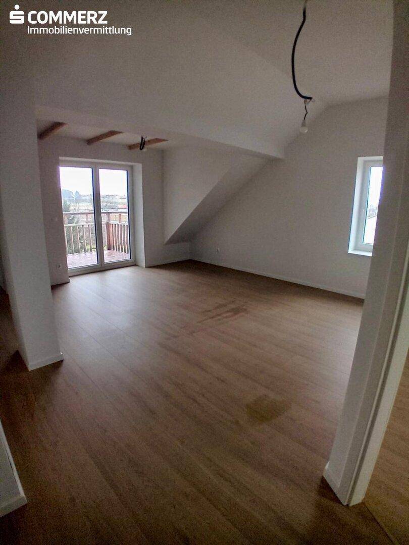 Geräumiger Raum mit Laminatboden, Zugang zu einem Balkon und schrägen Decken im Dachgeschoss.