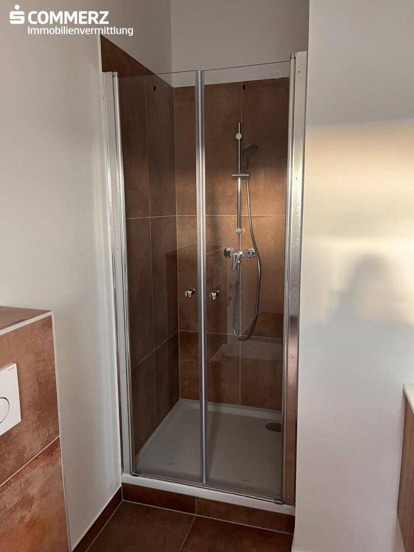 Badezimmer mit Duschkabine, braunen Fliesen an Wänden und Boden sowie moderner Armatur.