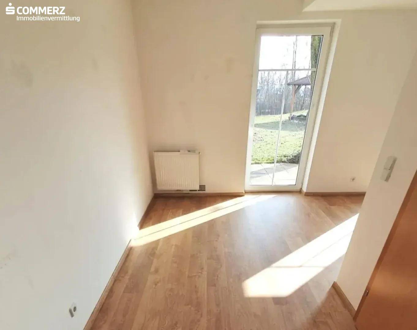 Heller, leerer Raum mit Laminatboden und Zugang zum Garten durch eine große Tür.