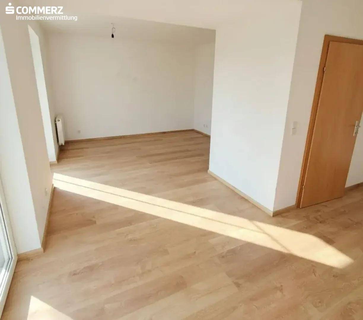 Lichtdurchfluteter, leerer Raum mit Laminatboden und weiß gestrichenen Wänden.