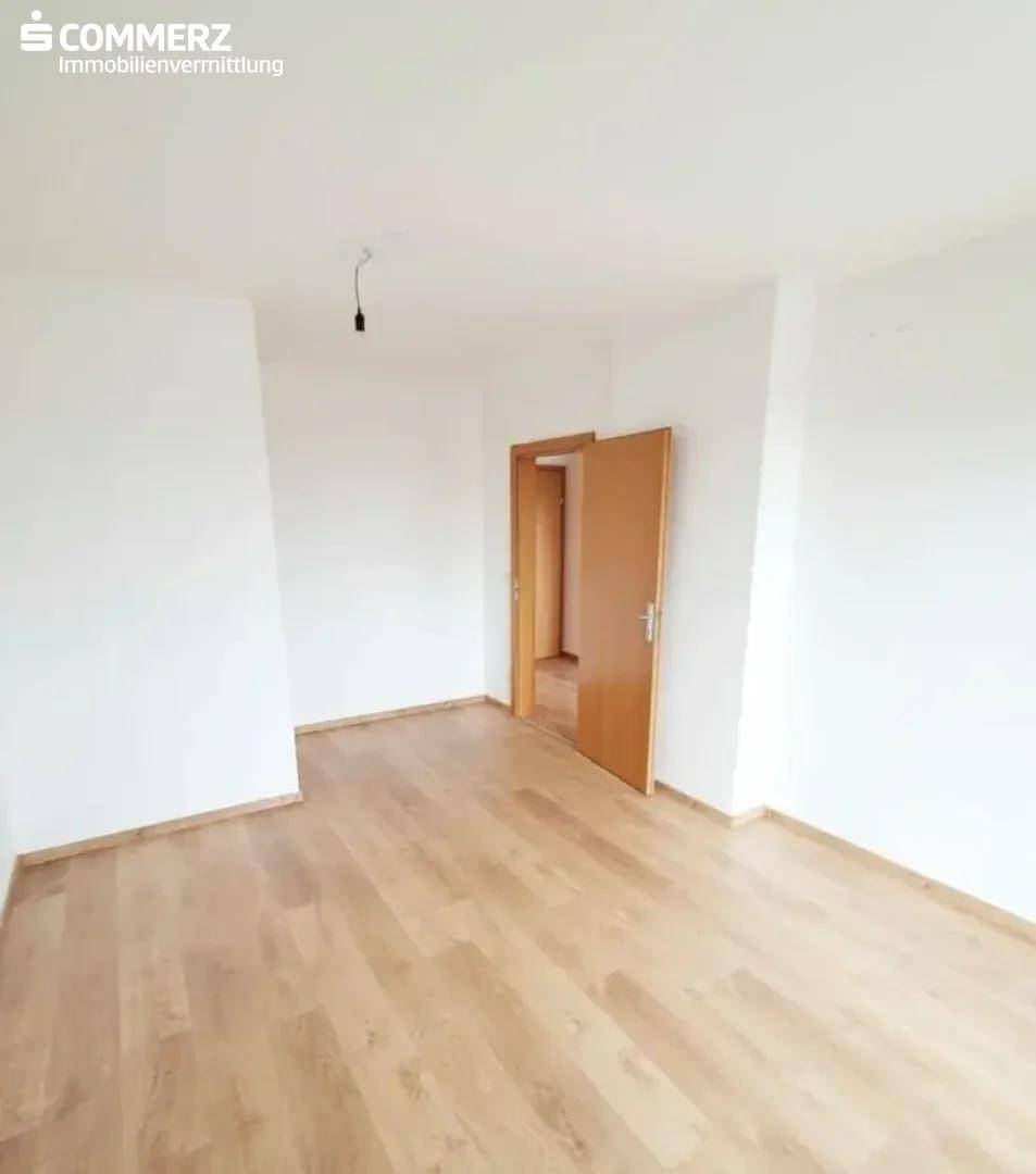 Geräumiger, leerer Raum mit Laminatboden und einer Holztür, bereit zur individuellen Gestaltung.