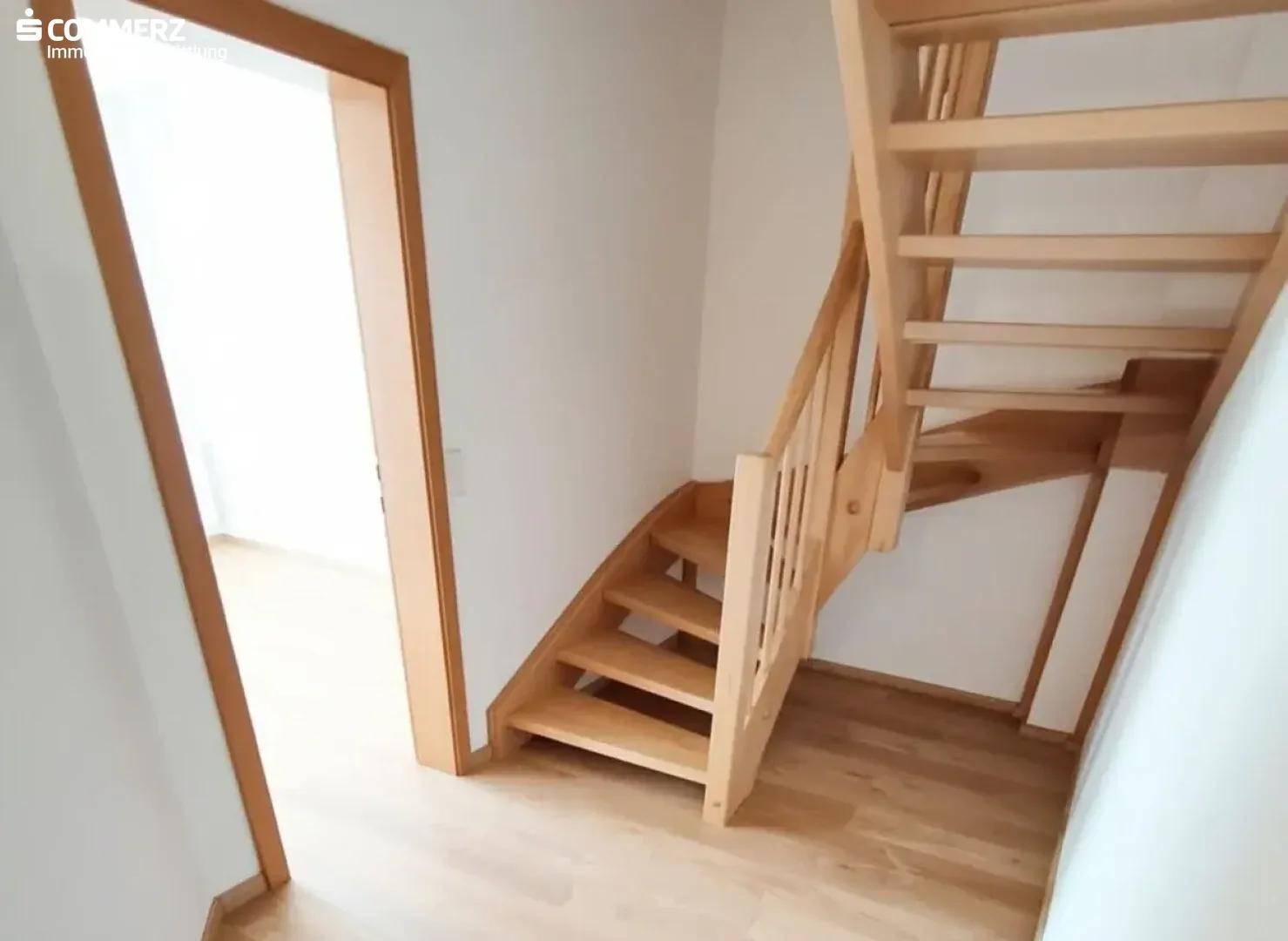 Heller Flur mit Holztreppe und Laminatboden, der die verschiedenen Ebenen verbindet.