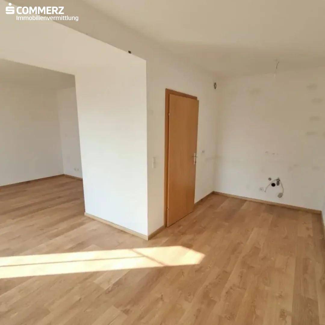 Leerer Raum mit Laminatboden und Anschlüssen an der Wand, möglicherweise für eine Küche.