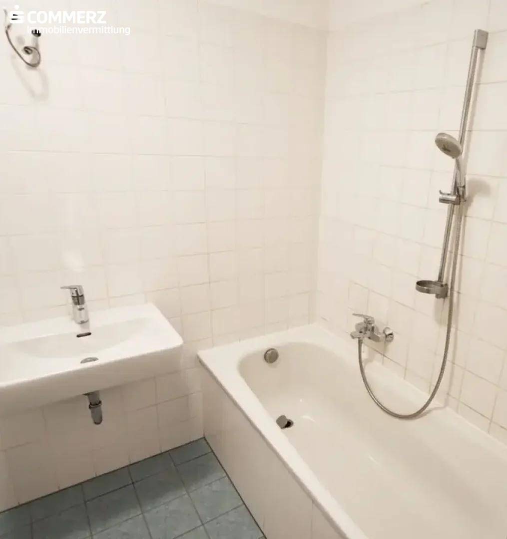 Helles Badezimmer mit weiß gefliesten Wänden, Badewanne und Waschbecken.