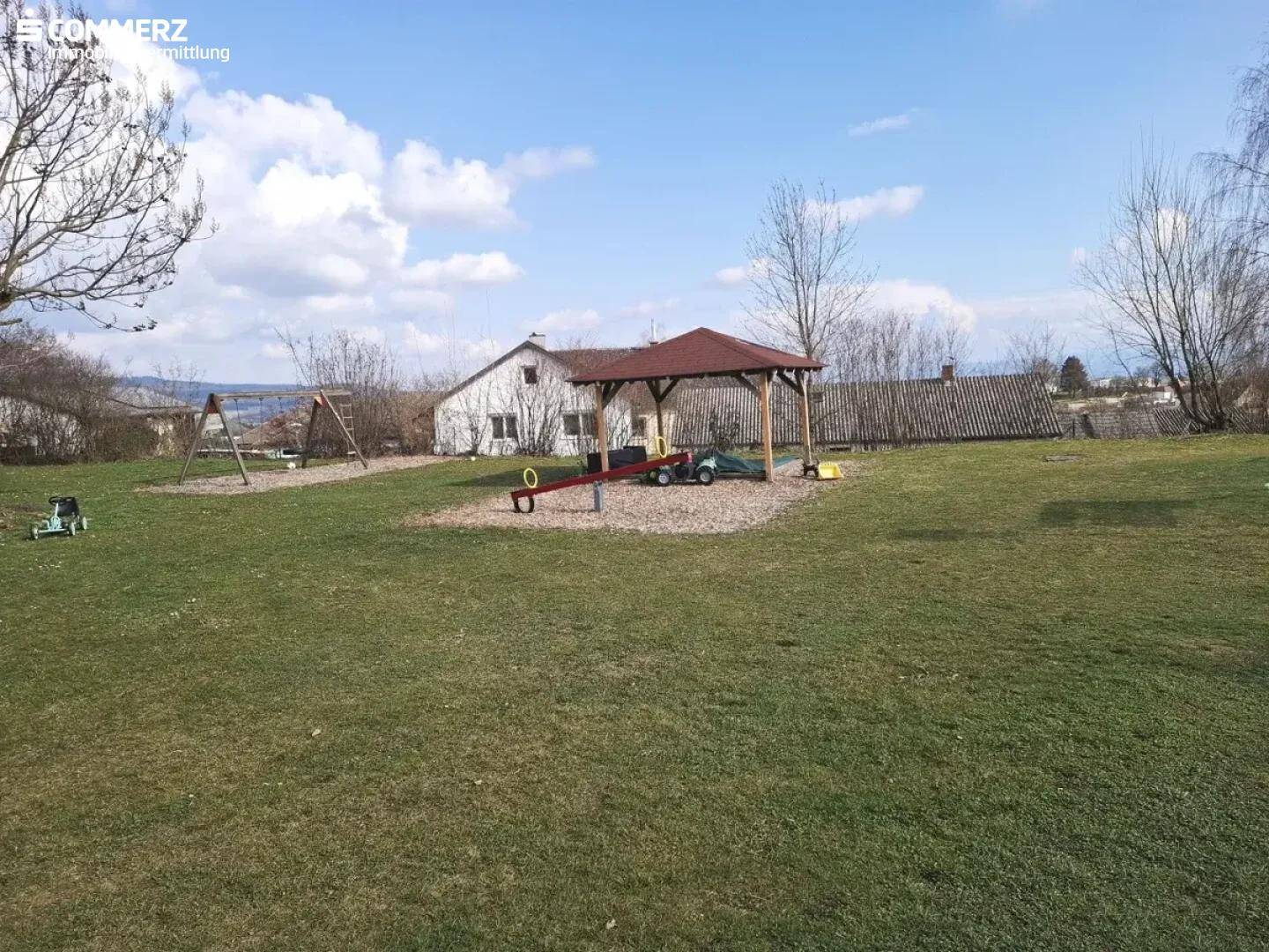 Großer Gartenbereich mit Spielplatz, Schaukeln und Wippe, ideal für Kinder.