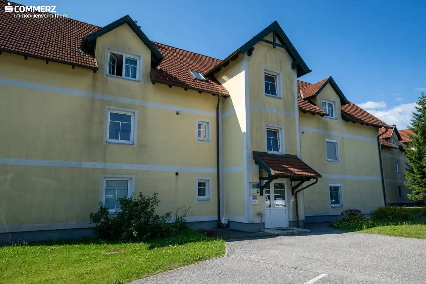 Ansicht eines Mehrfamilienhauses mit gelber Fassade, Satteldach und gepflegtem Eingangsbereich.