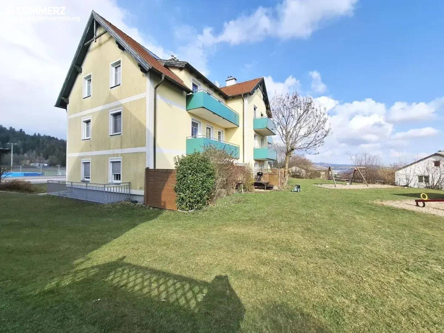 Mehrfamilienhaus mit gelber Fassade, Balkonen und großem Rasenbereich im Vordergrund.