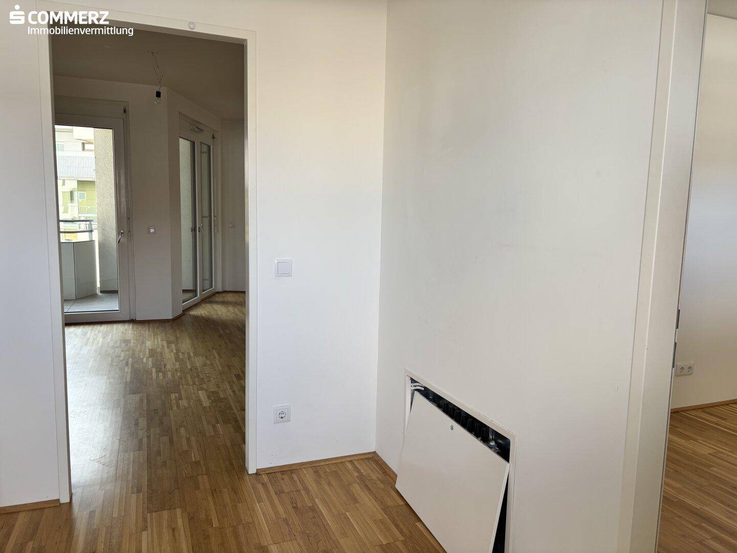 Heller Flur mit Parkettboden und Zugang zu einem Balkon, bereit zur individuellen Gestaltung.