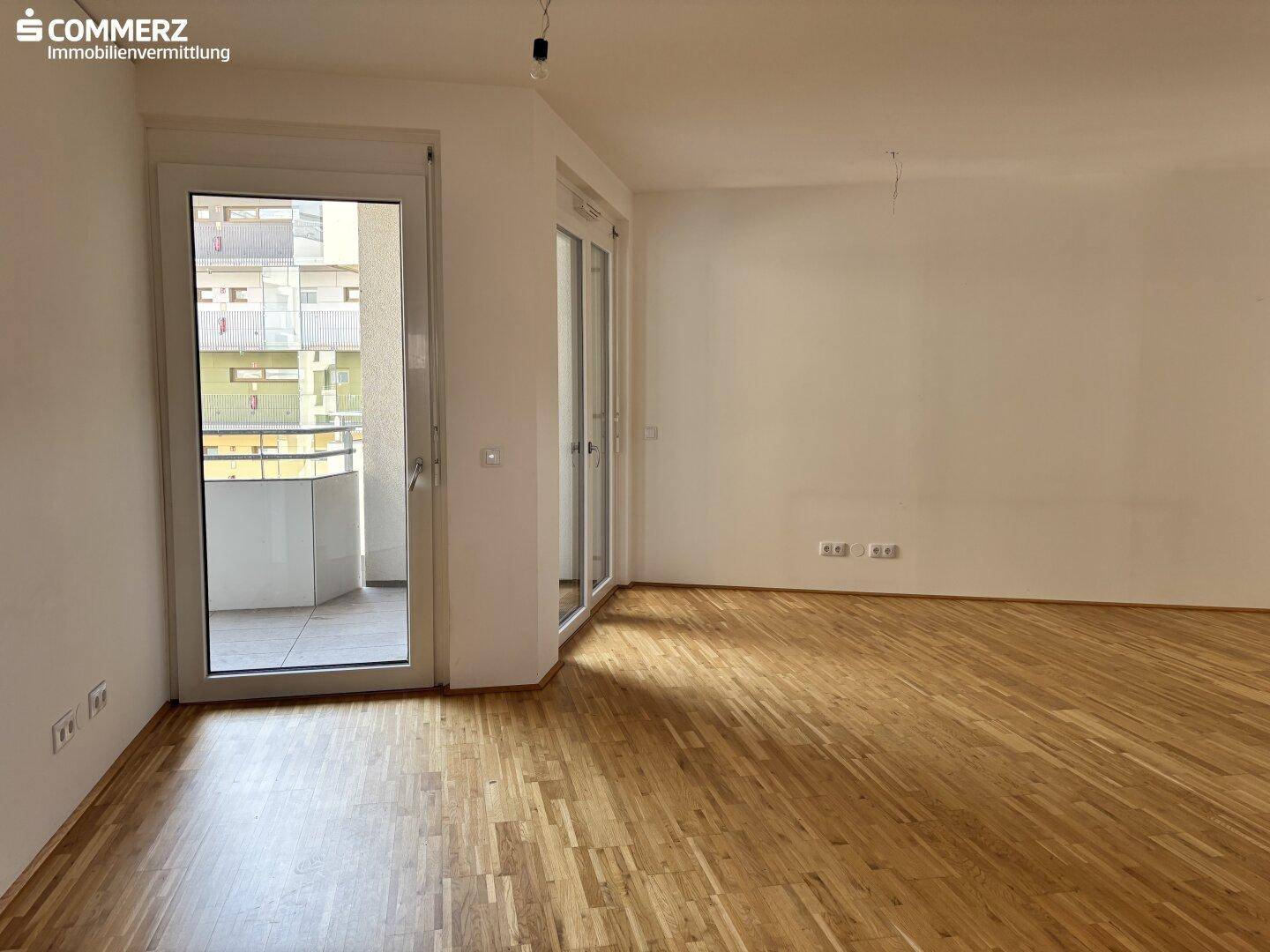 Geräumiges Wohnzimmer mit Parkettboden und großem Balkonzugang, lichtdurchflutet.