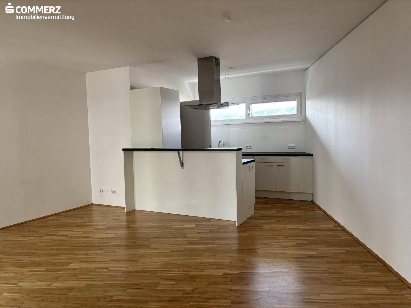 Offene Küche mit Kücheninsel, Dunstabzugshaube und Fenster, bereit für die Installation von Geräten.