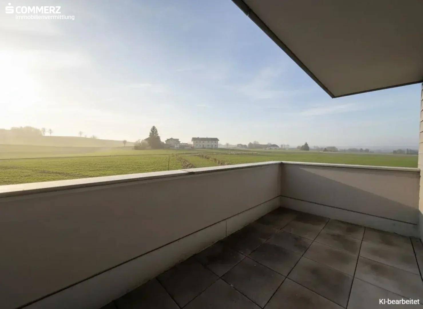 Unmöblierter Balkon mit Fliesenboden und weitem Blick über grüne Felder.