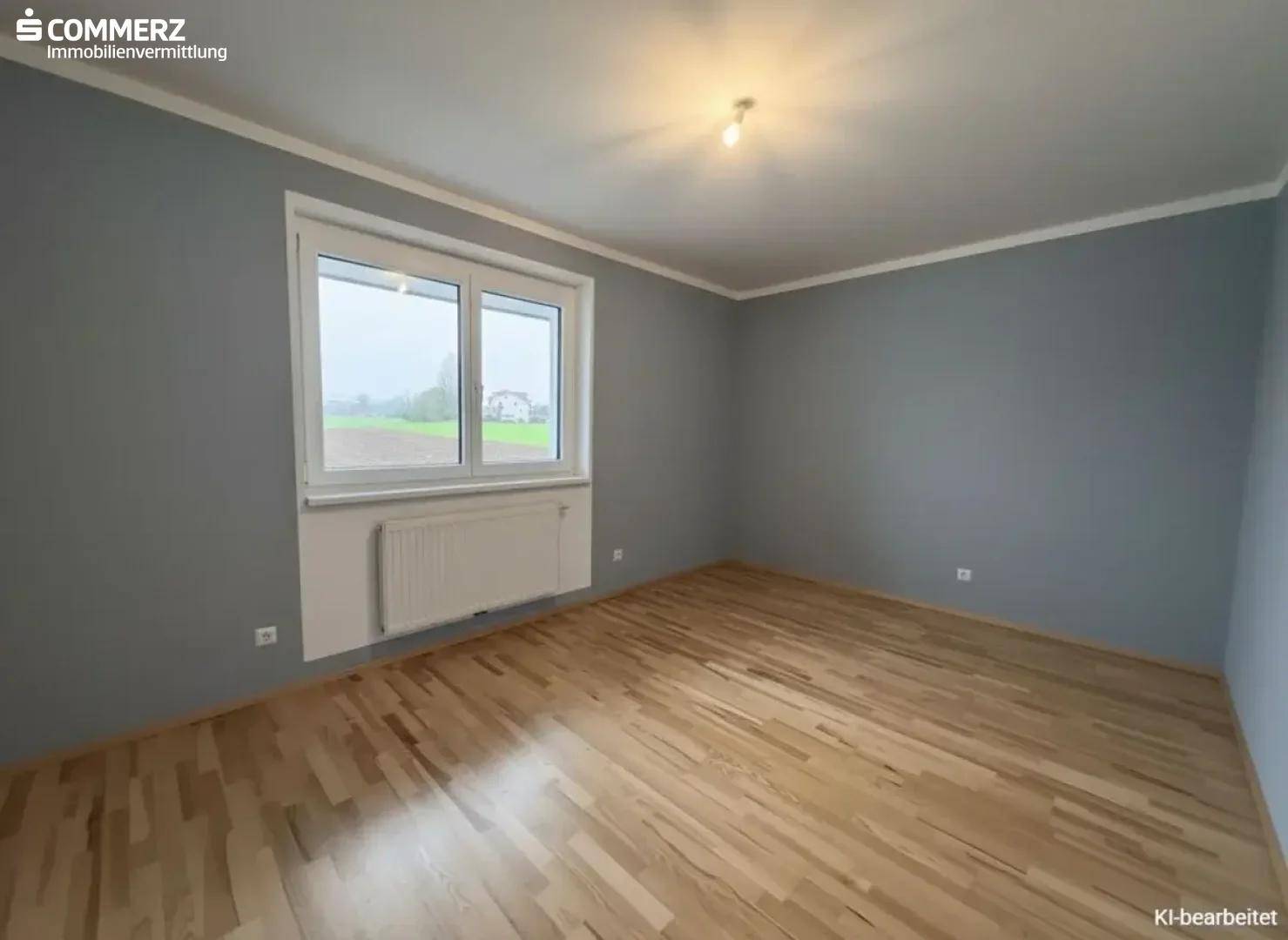Schlafzimmer mit grau gestrichenen Wänden und hellem Holzboden, bietet Blick ins Grüne.