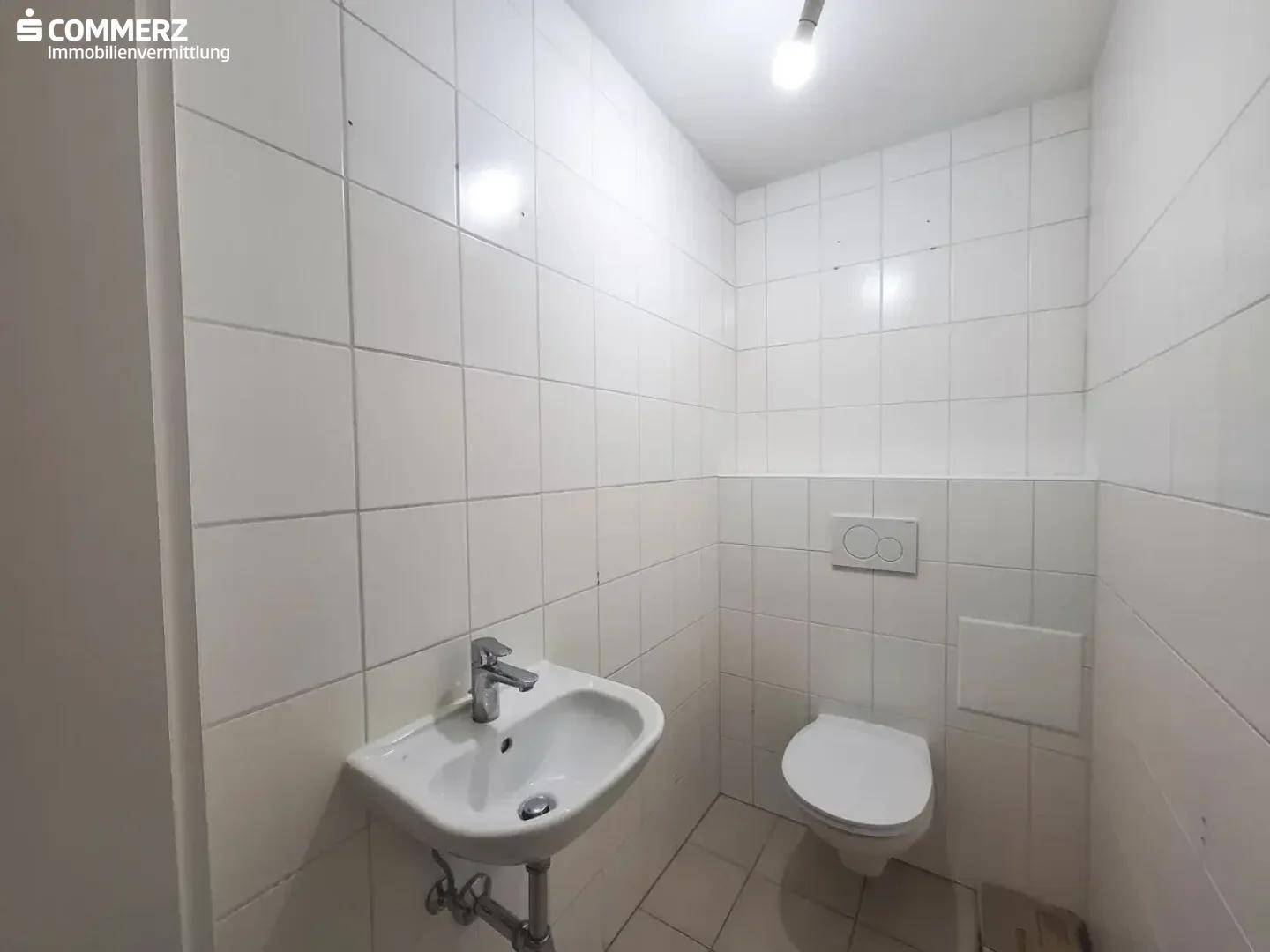 Kleines Gäste-WC mit weißen Fliesen, Wand-WC und Handwaschbecken.