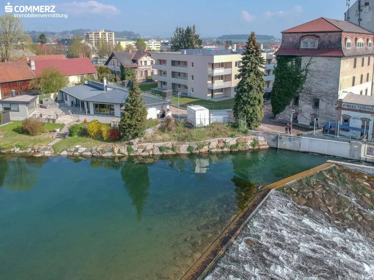 Luftaufnahme eines modernen Wohnkomplexes am Wasser mit umliegender Bebauung und Grünflächen.