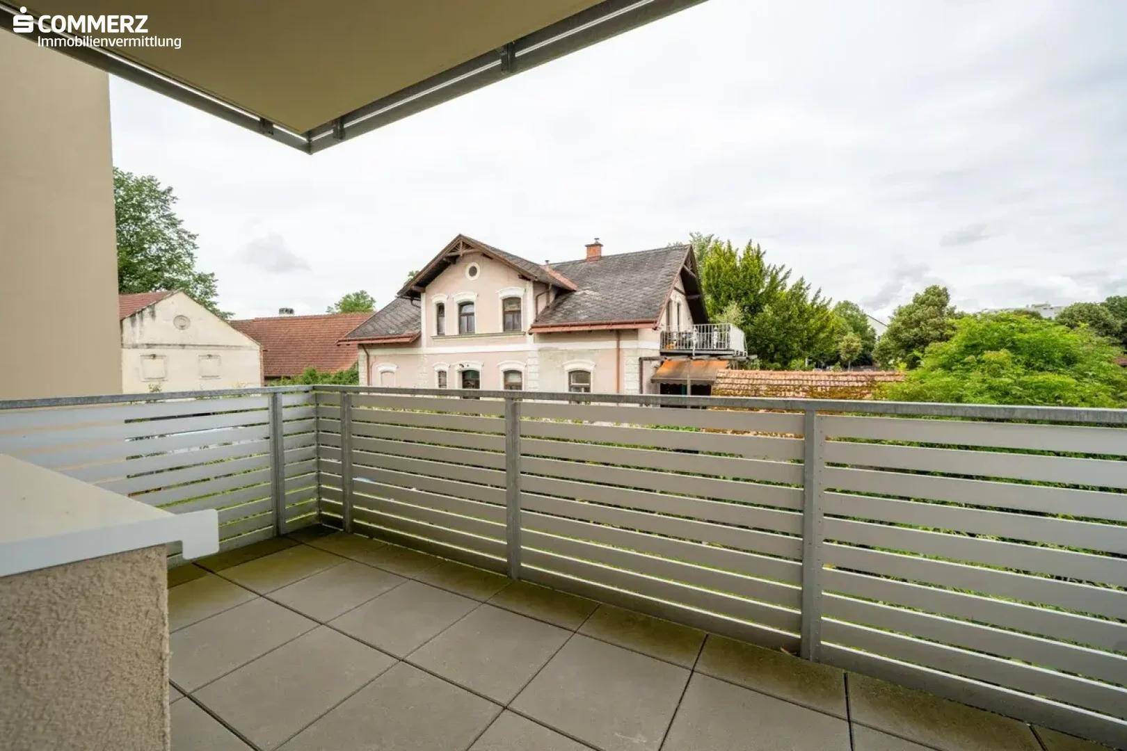 Geräumiger Balkon mit Fliesenboden und moderner grauer Brüstung, Blick auf umliegende Häuser.